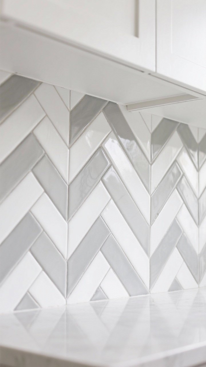 Detail closeup of a herringbone backsplash layout using elongated 2x8 white tiles with contrasting medium-gray grout to emphasize the zig-zag pattern. Show the pattern running vertically for height near the underside of white cabinets. Include a sliver of light countertop edge; crisp, bright lighting; photorealistic.